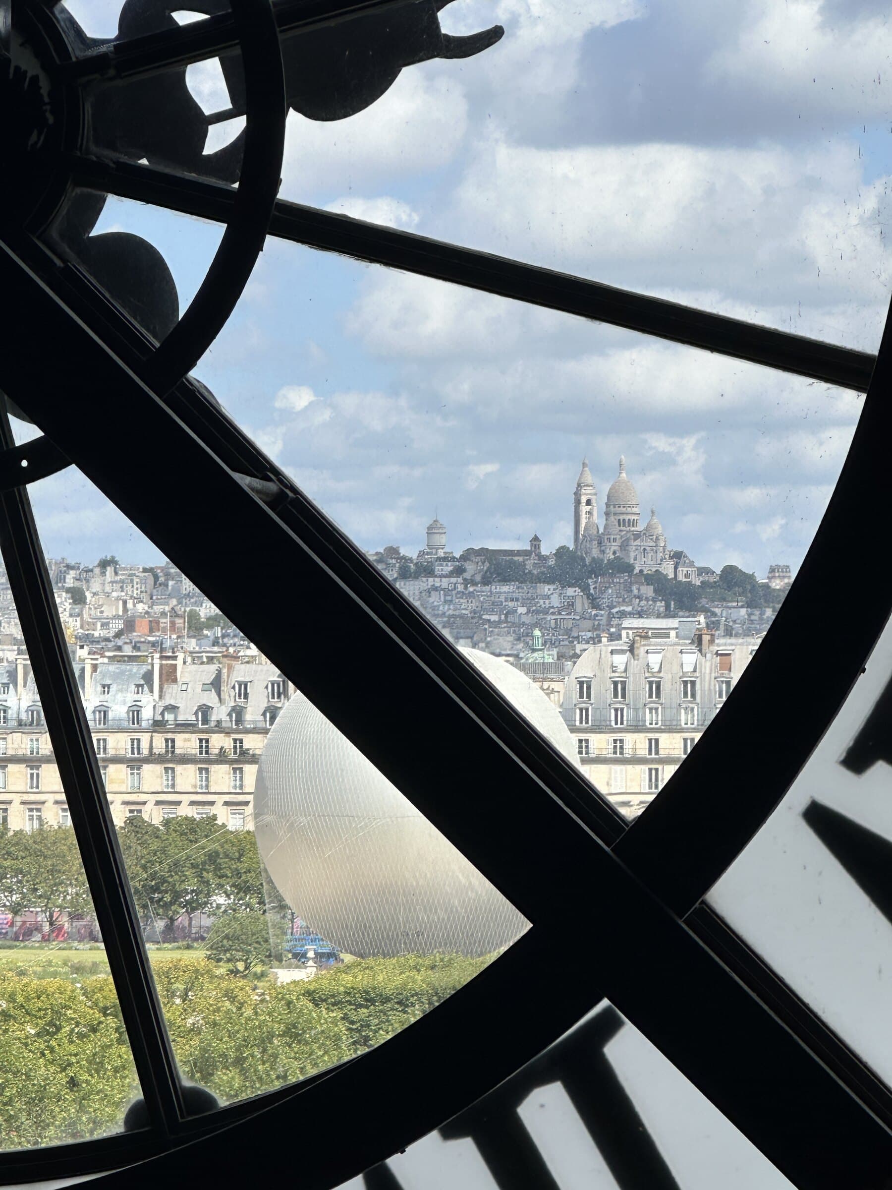 Paris clock window framing Sacre-Coeur in the distance.