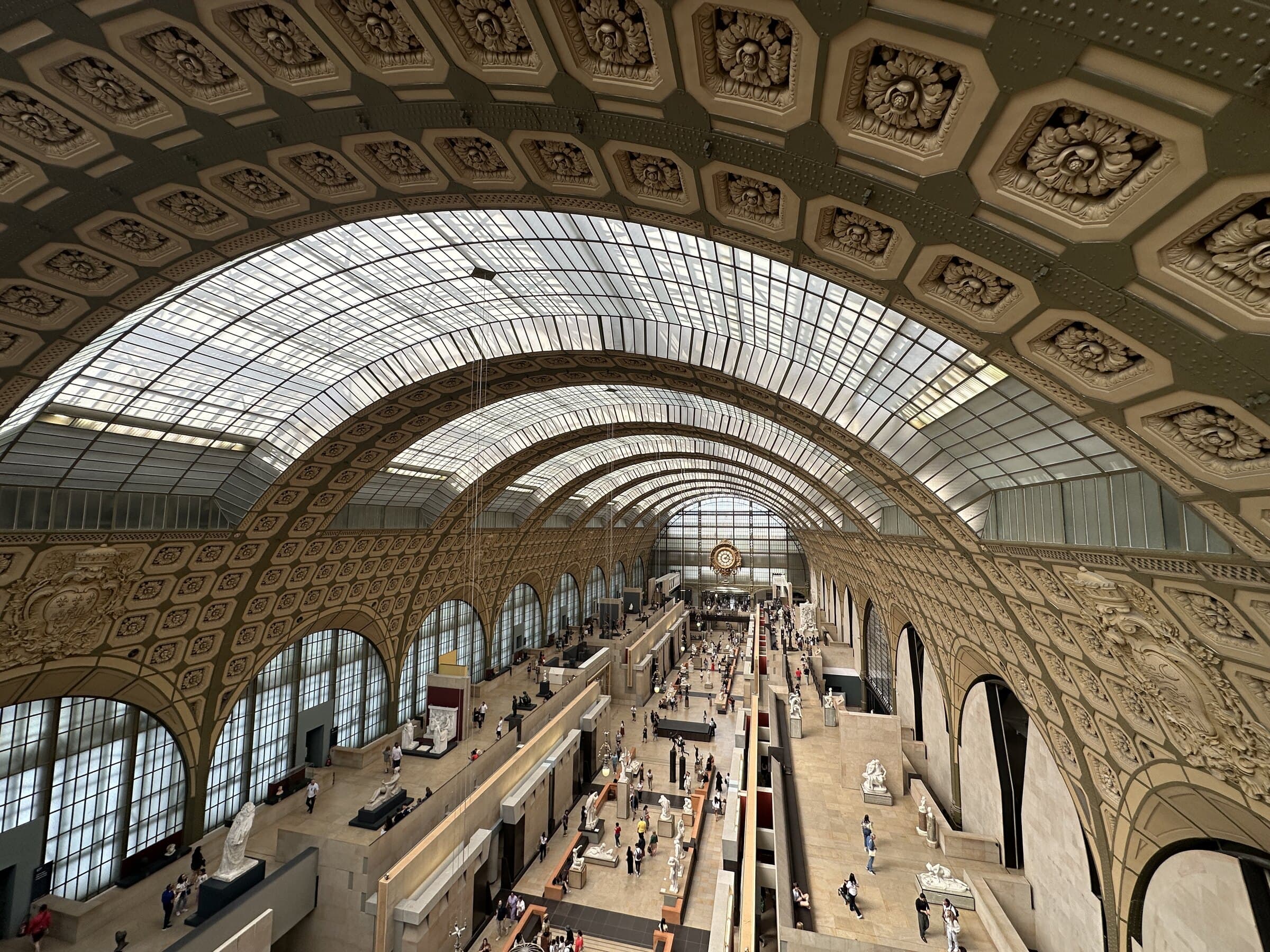 Grand Paris hall with visitors beneath a vaulted glass roof.